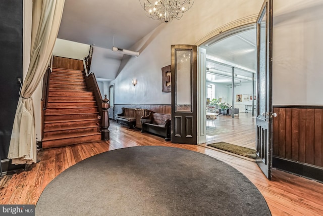 foyer entrance featuring a wainscoted wall, stairway, wood finished floors, and an inviting chandelier