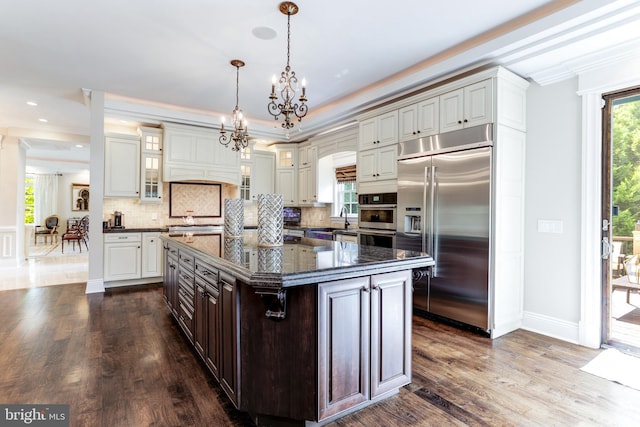 kitchen with tasteful backsplash, a chandelier, built in refrigerator, a center island, and dark brown cabinetry