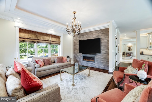 living room featuring a large fireplace, ornamental molding, a raised ceiling, a notable chandelier, and hardwood / wood-style flooring