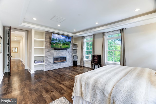 bedroom featuring dark hardwood / wood-style flooring, a raised ceiling, and a stone fireplace