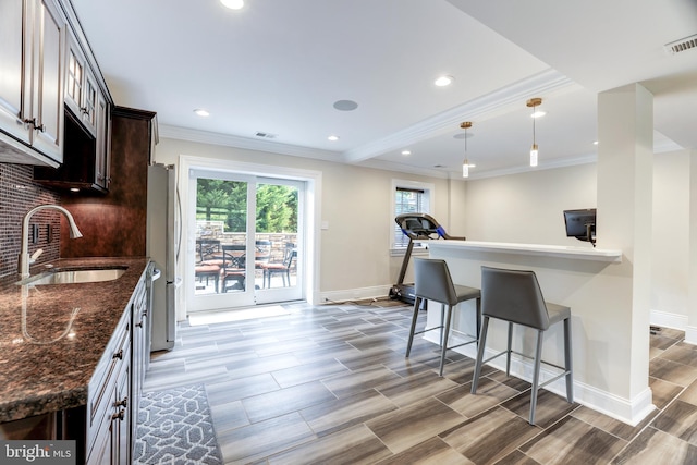 kitchen with dark brown cabinetry, sink, a breakfast bar area, dark stone countertops, and backsplash