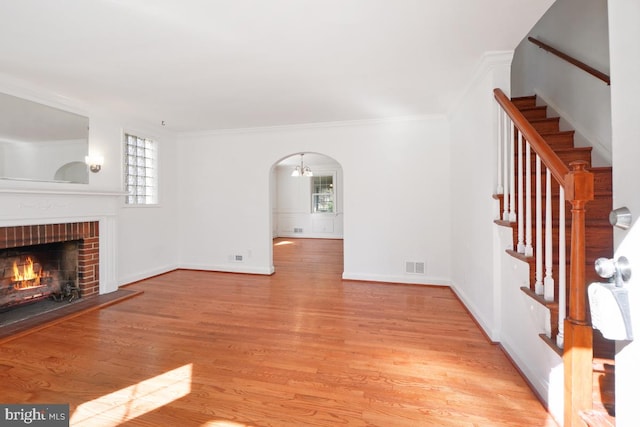 unfurnished living room with ornamental molding, a brick fireplace, and light wood-type flooring