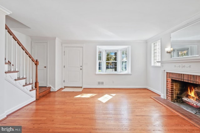 unfurnished living room with ornamental molding, a brick fireplace, and light wood-type flooring