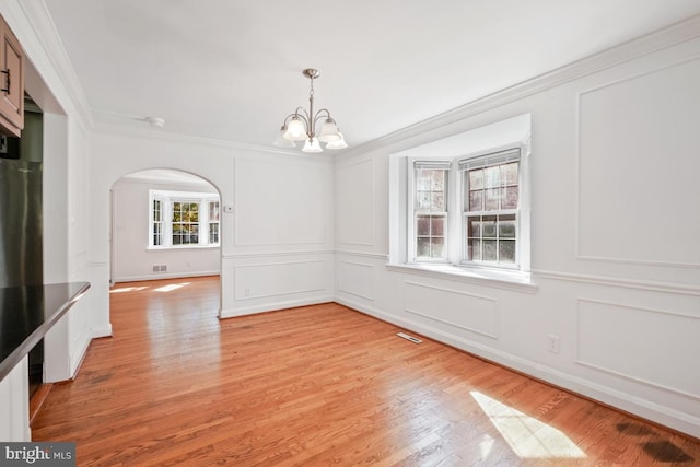 unfurnished dining area with an inviting chandelier, ornamental molding, and light hardwood / wood-style floors