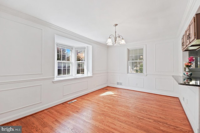 unfurnished dining area with an inviting chandelier, ornamental molding, and light hardwood / wood-style floors