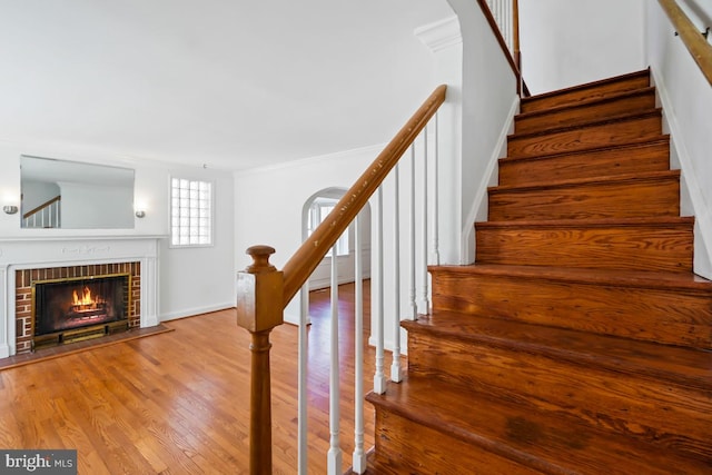 stairway with hardwood / wood-style flooring, ornamental molding, and a brick fireplace