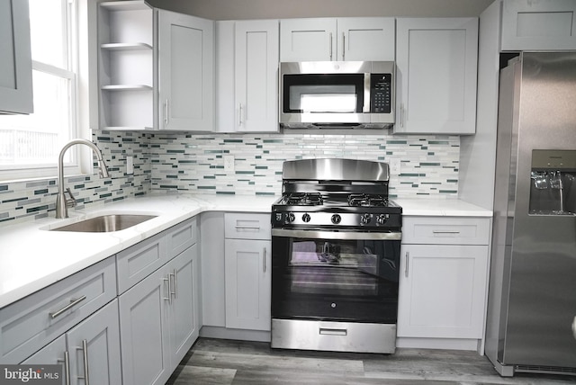 kitchen with hardwood / wood-style flooring, decorative backsplash, sink, appliances with stainless steel finishes, and gray cabinetry