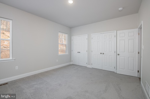 unfurnished bedroom featuring multiple closets and light colored carpet