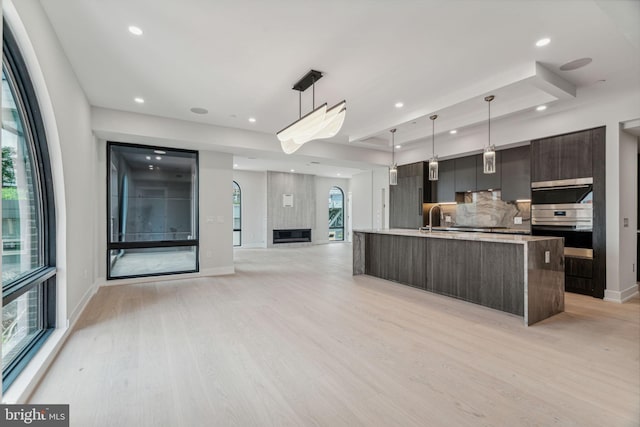 kitchen with pendant lighting, light wood-type flooring, dark brown cabinets, and a center island with sink