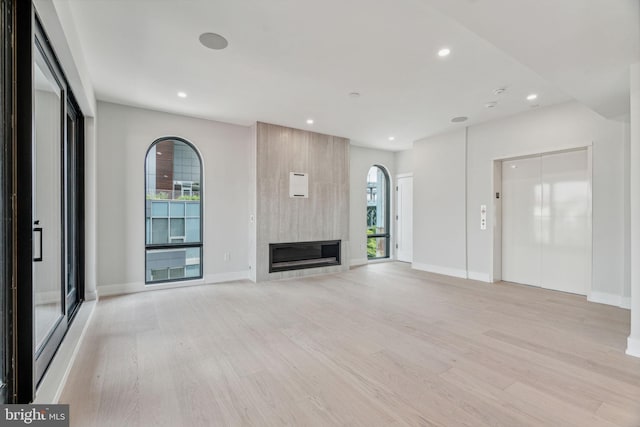 unfurnished living room featuring light hardwood / wood-style floors, a large fireplace, and elevator