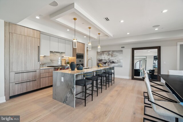 kitchen featuring light stone counters, light hardwood / wood-style flooring, hanging light fixtures, white cabinets, and a spacious island