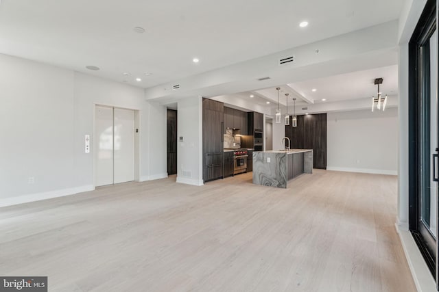 unfurnished living room with a raised ceiling, sink, elevator, and light hardwood / wood-style floors