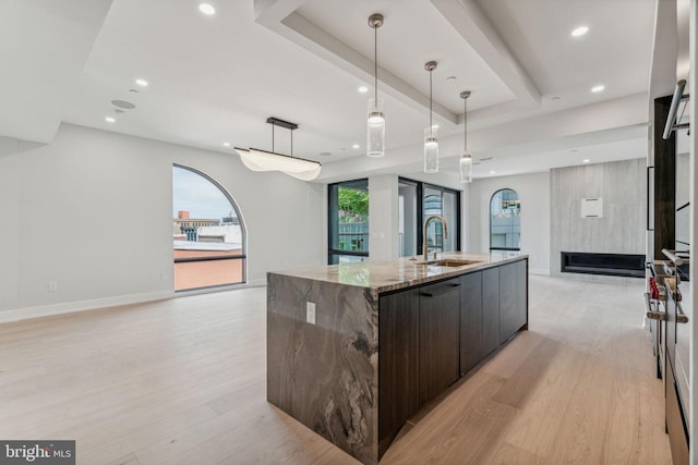 kitchen featuring a large island, sink, pendant lighting, dark brown cabinetry, and light stone counters