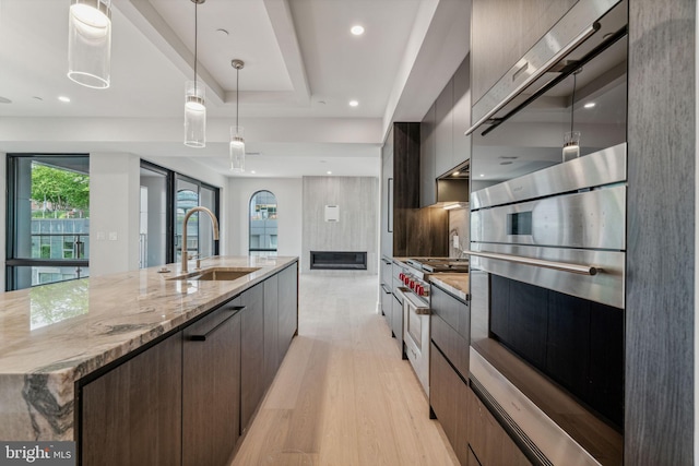 kitchen featuring appliances with stainless steel finishes, pendant lighting, sink, light stone countertops, and light wood-type flooring