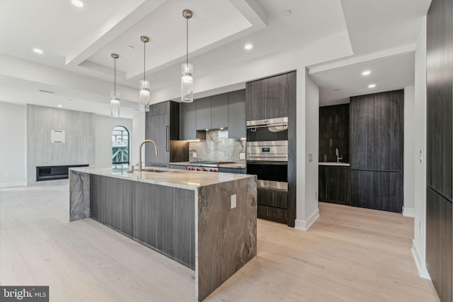 kitchen featuring sink, decorative light fixtures, light hardwood / wood-style flooring, a raised ceiling, and a large island