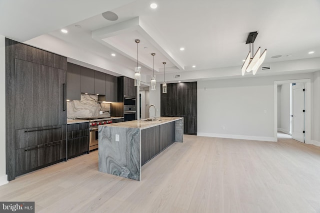 kitchen with pendant lighting, a spacious island, high end range, and light hardwood / wood-style flooring