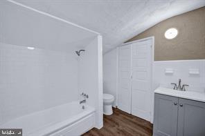 full bathroom with toilet,  shower combination, tile walls, vanity, and hardwood / wood-style floors