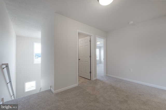 spare room featuring light carpet, a textured ceiling, and baseboards