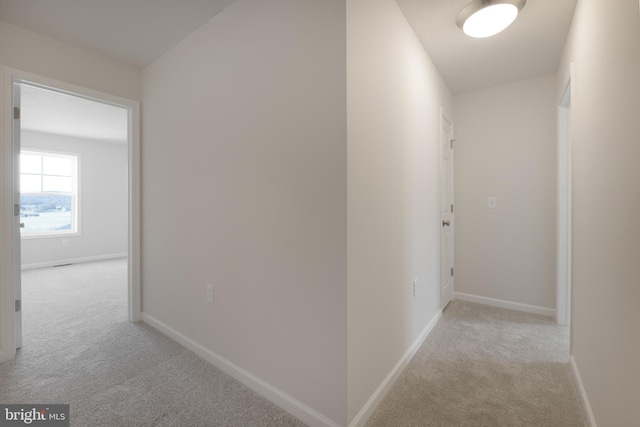 hallway featuring light carpet and baseboards