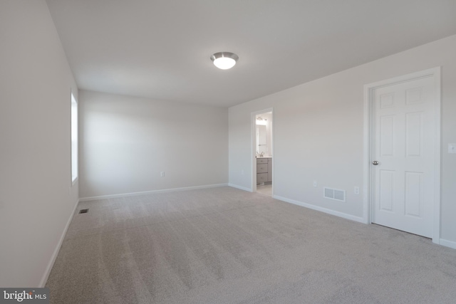 unfurnished bedroom with light carpet, ensuite bathroom, visible vents, and baseboards