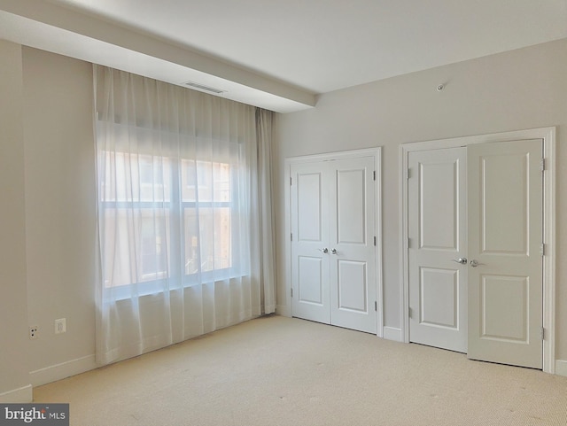 unfurnished bedroom featuring multiple closets and light colored carpet