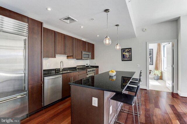 kitchen featuring premium appliances, dark stone countertops, a center island, dark hardwood / wood-style floors, and sink