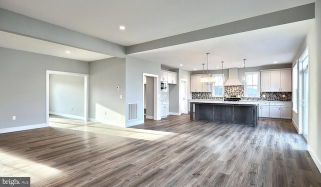 kitchen featuring tasteful backsplash, hardwood / wood-style flooring, custom range hood, a kitchen island, and pendant lighting