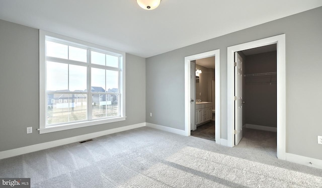 unfurnished bedroom featuring connected bathroom, a walk in closet, light colored carpet, and a closet