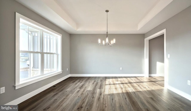 unfurnished dining area with an inviting chandelier, hardwood / wood-style floors, and a tray ceiling