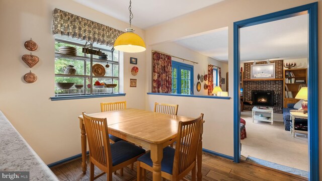 dining room featuring plenty of natural light, brick wall, a brick fireplace, and hardwood / wood-style floors