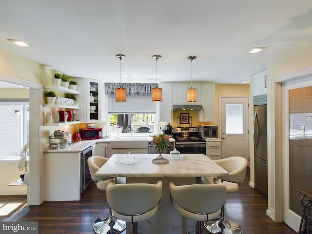 kitchen featuring dark wood-type flooring, hanging light fixtures, stainless steel appliances, sink, and a center island