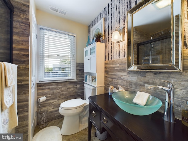 bathroom with vanity, toilet, tile walls, and a shower with door