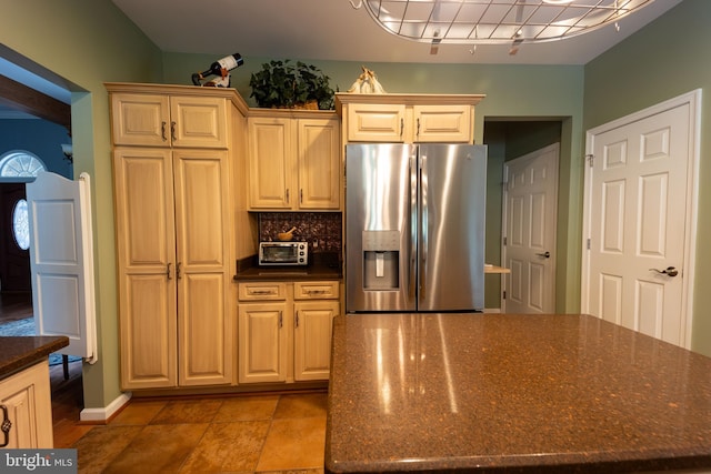 kitchen featuring dark stone counters, backsplash, rail lighting, tile patterned floors, and stainless steel fridge