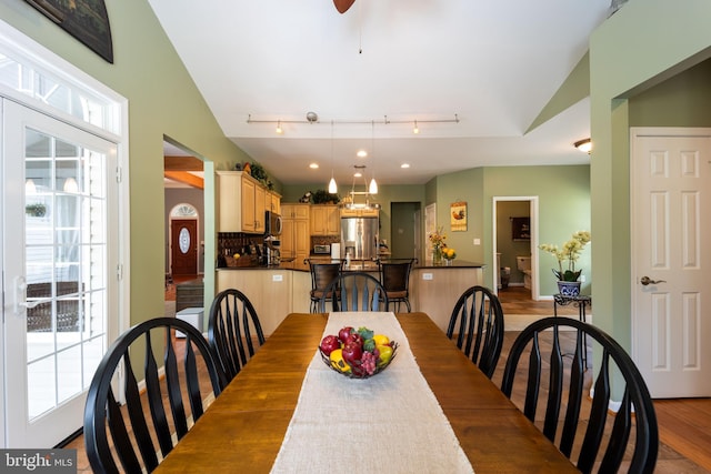 dining space with a wealth of natural light, vaulted ceiling, rail lighting, and hardwood / wood-style flooring