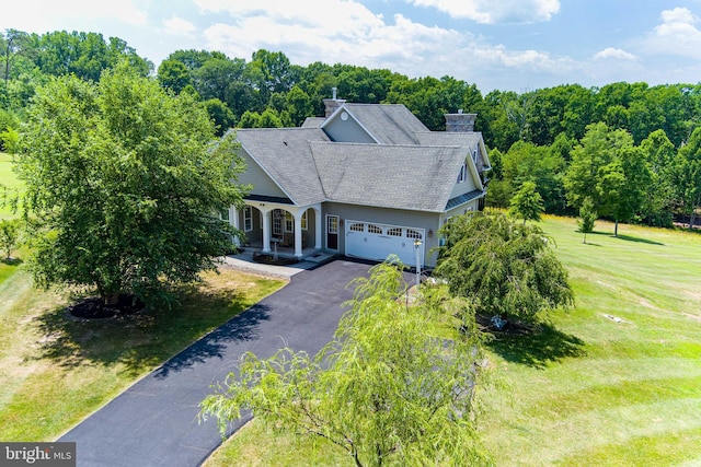 view of front facade featuring aphalt driveway, a garage, a shingled roof, a chimney, and a front yard