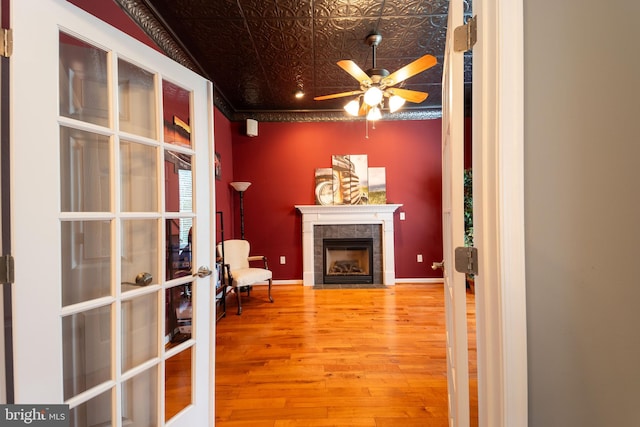 interior space featuring wood-type flooring, french doors, a tiled fireplace, ceiling fan, and crown molding