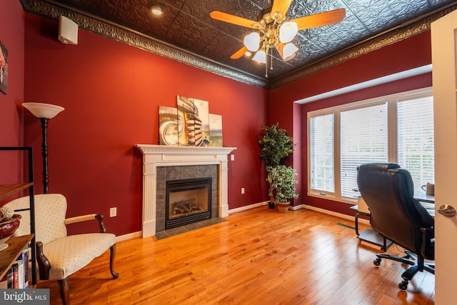 home office with ceiling fan, light hardwood / wood-style flooring, crown molding, and a tiled fireplace