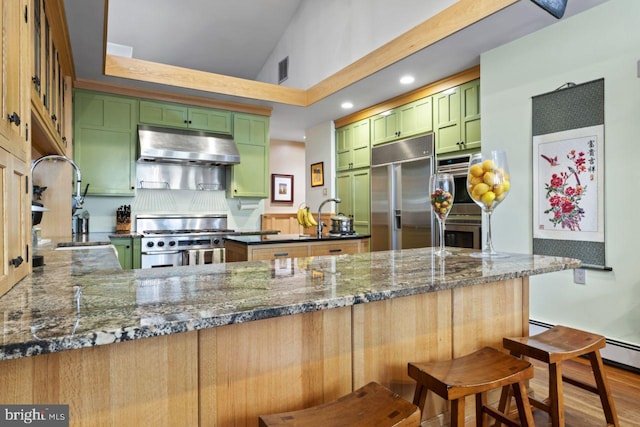 kitchen featuring hardwood / wood-style floors, dark stone countertops, high end appliances, green cabinetry, and a kitchen breakfast bar