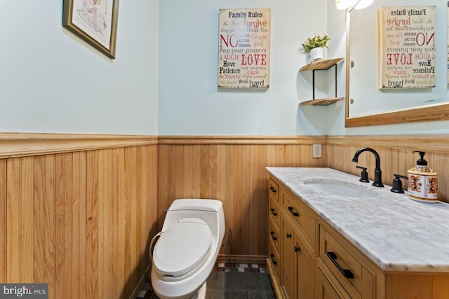 bathroom with wooden walls, tile patterned floors, toilet, and vanity