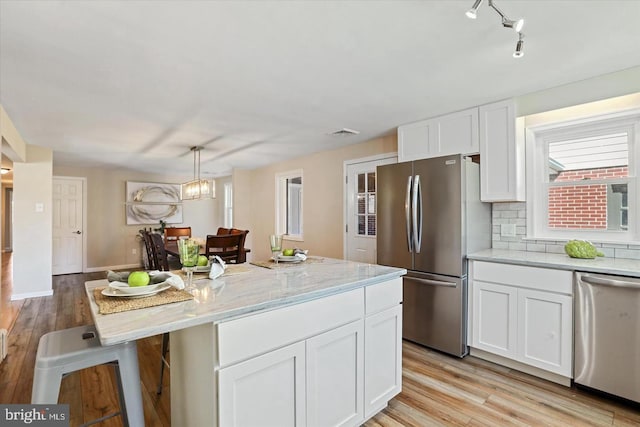 kitchen featuring a center island, pendant lighting, stainless steel appliances, light stone countertops, and white cabinets