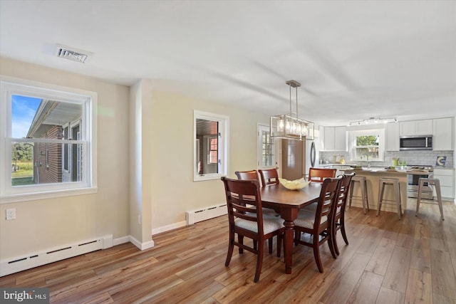 dining room featuring a notable chandelier, light hardwood / wood-style flooring, and a baseboard heating unit