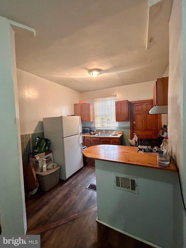 kitchen with range, kitchen peninsula, exhaust hood, white refrigerator, and dark hardwood / wood-style floors