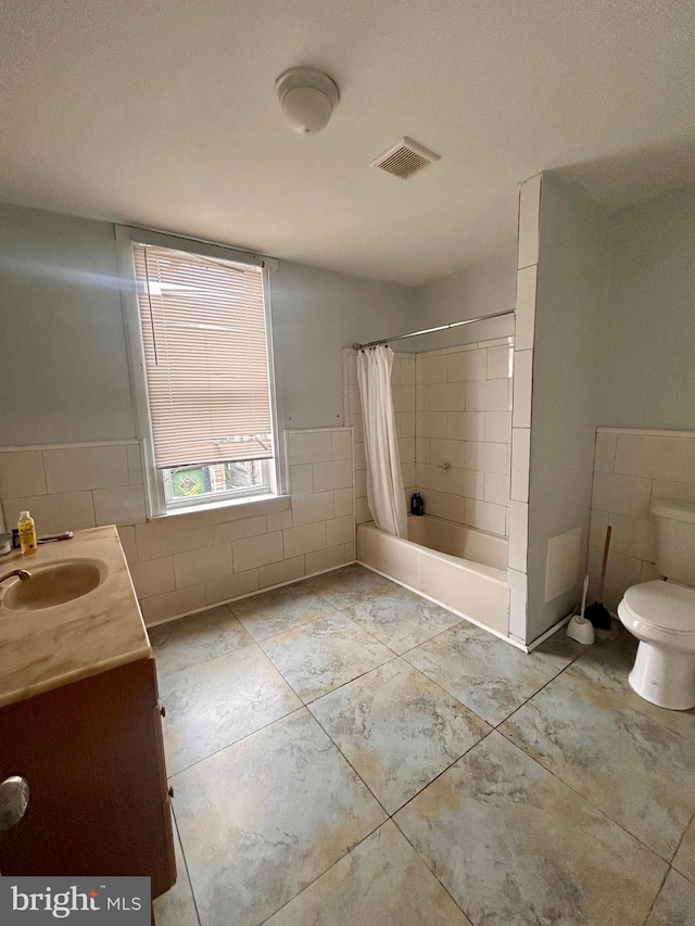 full bathroom featuring vanity, tile walls, shower / bath combo with shower curtain, and toilet