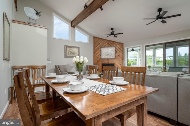 dining area featuring vaulted ceiling with beams, light hardwood / wood-style flooring, wooden walls, and ceiling fan