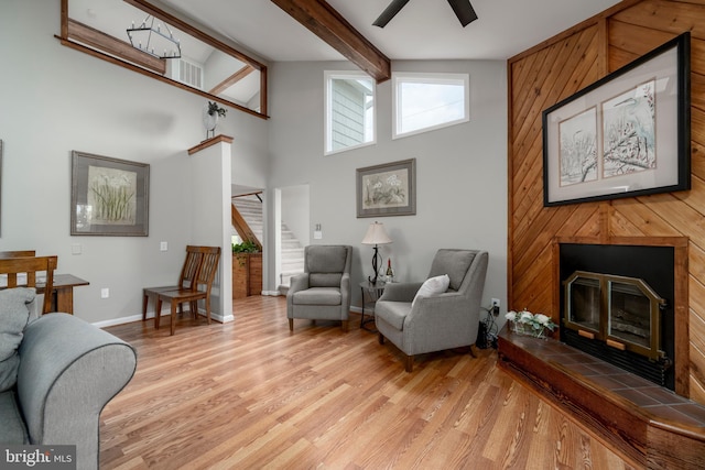 living room featuring beam ceiling, wooden walls, light wood-type flooring, high vaulted ceiling, and ceiling fan