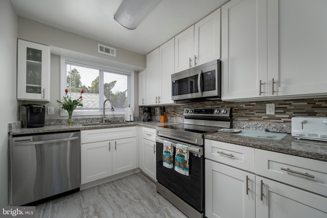 kitchen featuring decorative backsplash, white cabinets, appliances with stainless steel finishes, dark stone counters, and sink