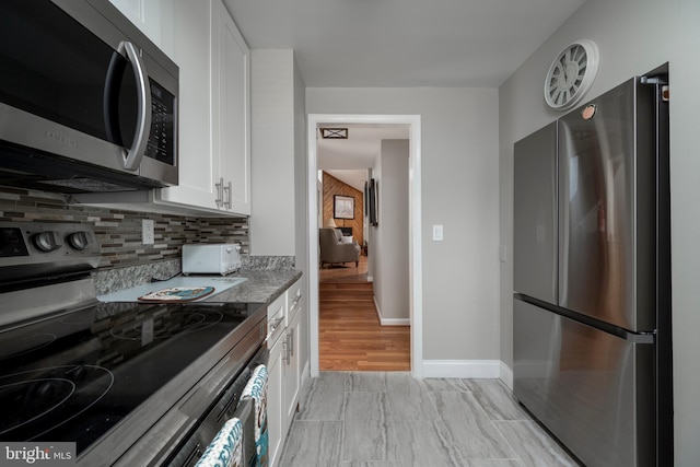 kitchen with stone counters, appliances with stainless steel finishes, backsplash, white cabinetry, and light hardwood / wood-style flooring