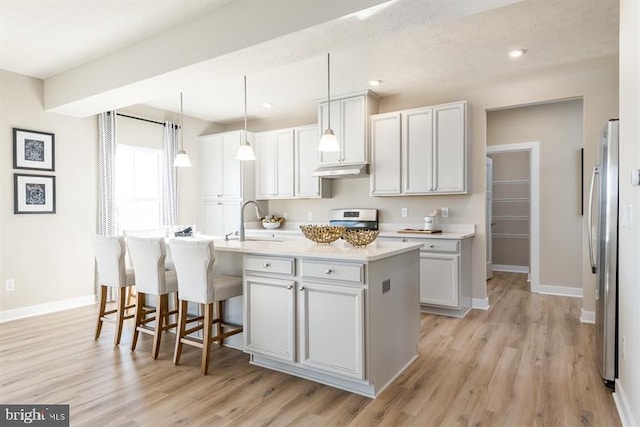 kitchen with sink, light hardwood / wood-style flooring, appliances with stainless steel finishes, a center island with sink, and decorative light fixtures