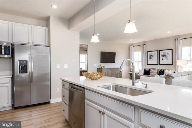 kitchen with sink, white cabinetry, stainless steel appliances, light hardwood / wood-style floors, and decorative light fixtures