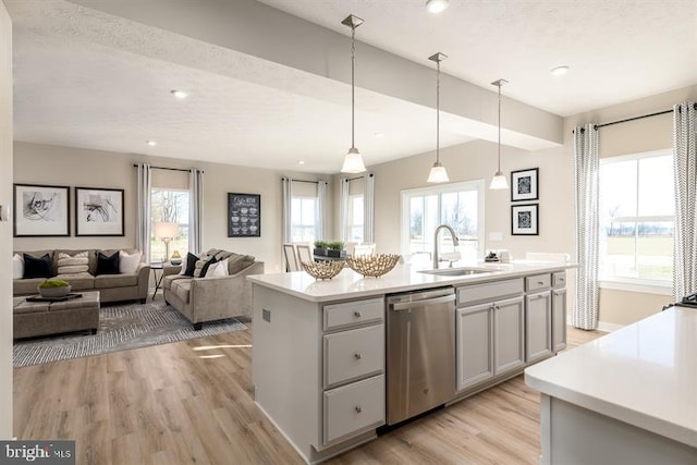 kitchen with sink, hanging light fixtures, a center island with sink, light wood-type flooring, and dishwasher